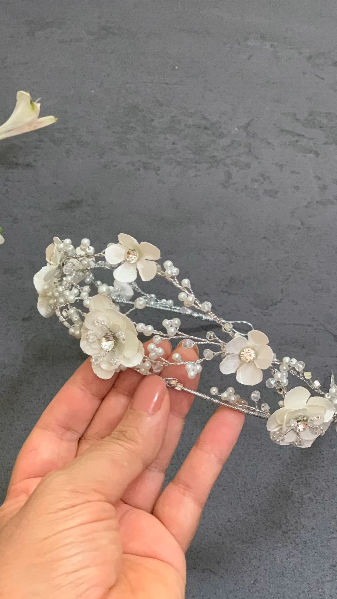 This may contain: a hand holding a white flower and crystal tiara on top of a gray surface