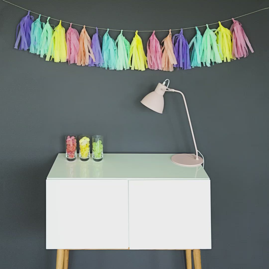 This may contain: a white table topped with a lamp and colorful tassels hanging from the ceiling