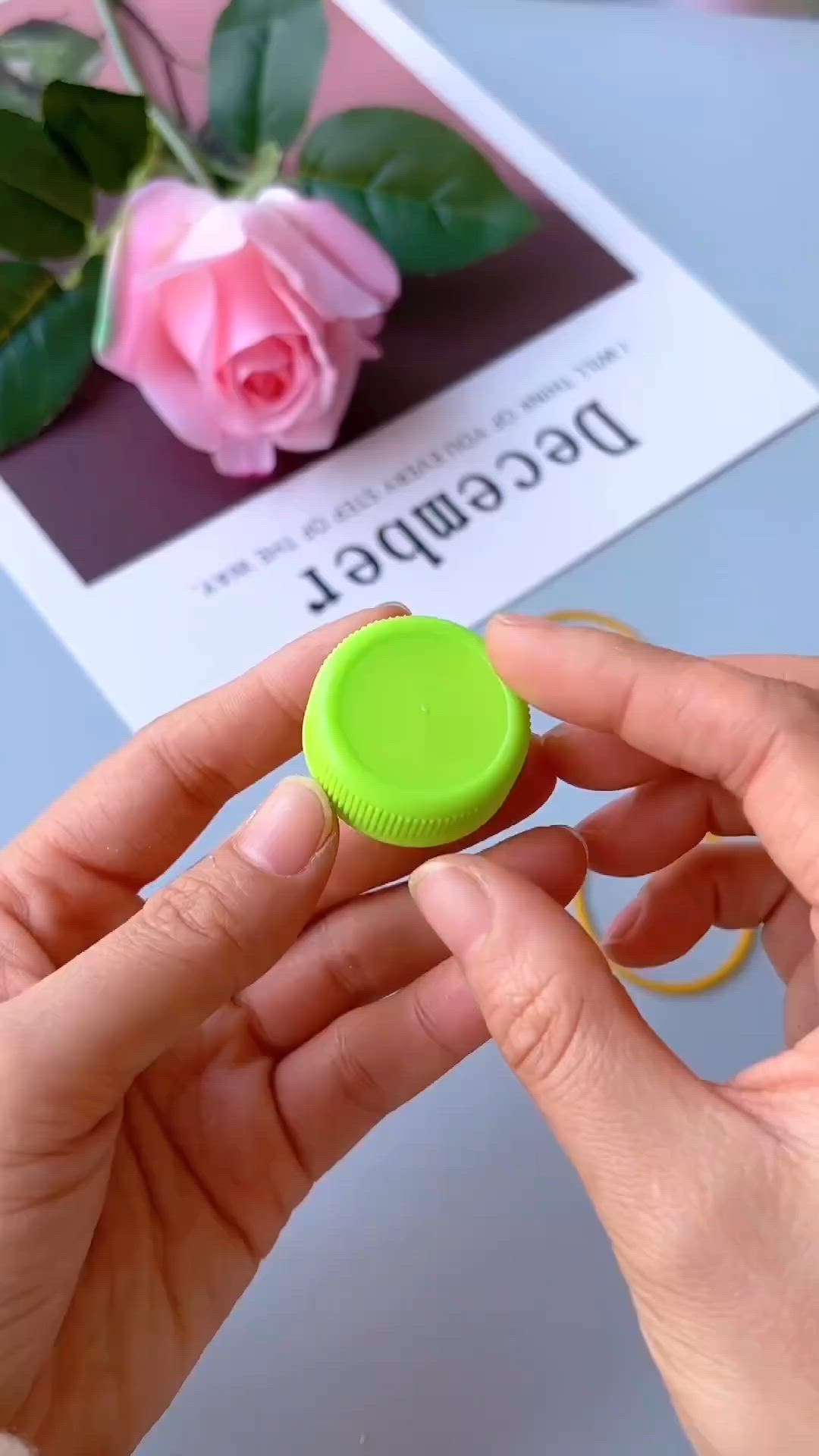 This may contain: a hand holding a green button with pink roses in the background on a white table