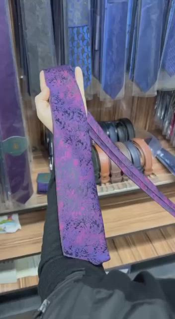 This may contain: a person holding up a purple tie in front of a shelf with ties on it