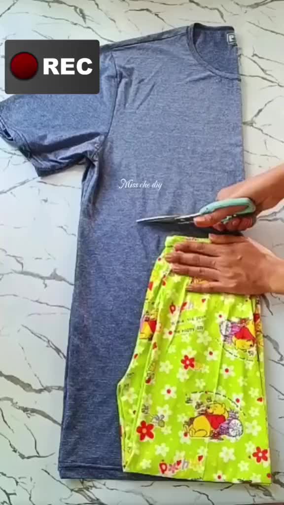 This may contain: a person cutting fabric with scissors on top of a table next to a t - shirt