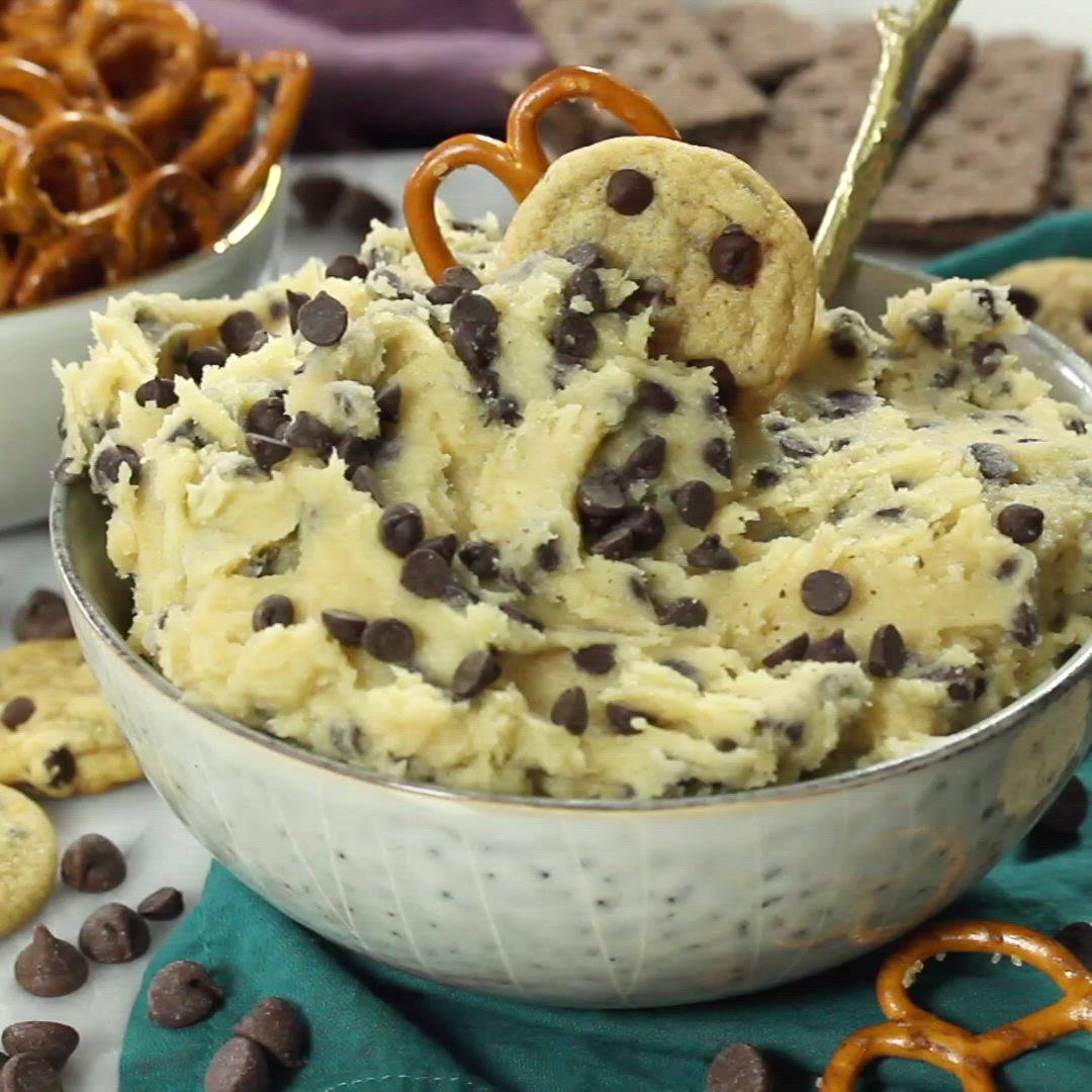 This may contain: chocolate chip cookie dough in a bowl with pretzels and pretzels on the side