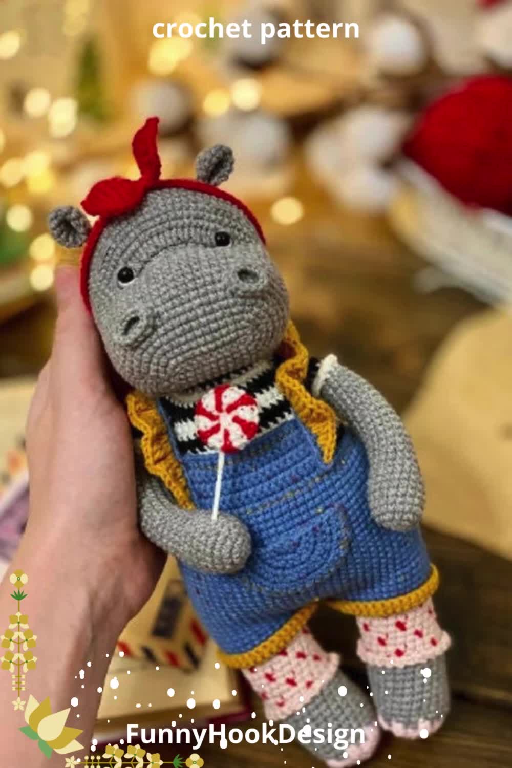 This may contain: a crocheted hippo is holding up a tiny stuffed animal with a red bow on it's head