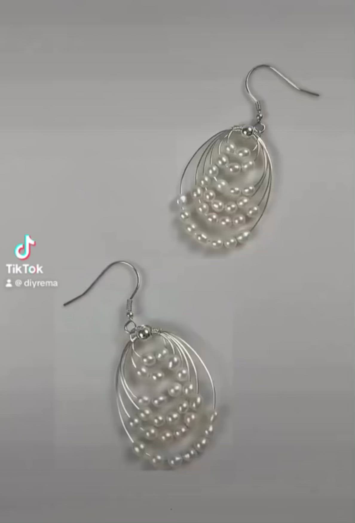 This may contain: pair of earrings with white pearls and silver wire hanging from the ear hooks on a gray background