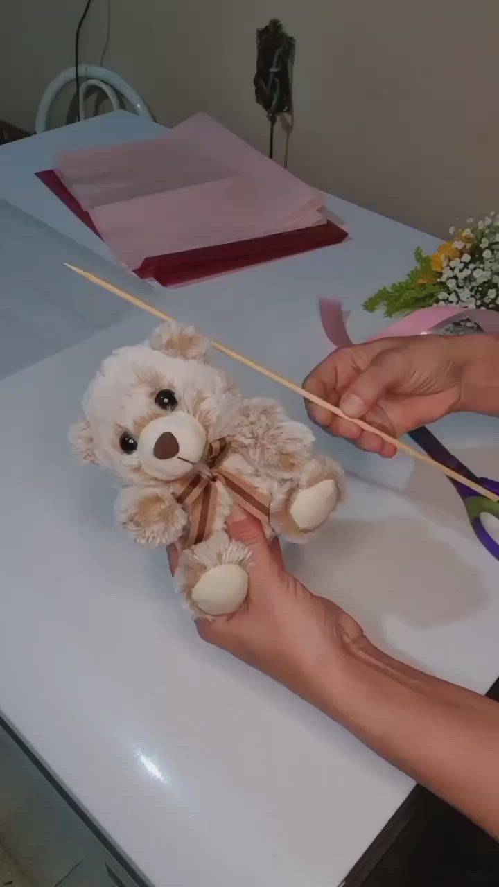 This may contain: a person holding a bouquet of flowers with a teddy bear on the table behind them