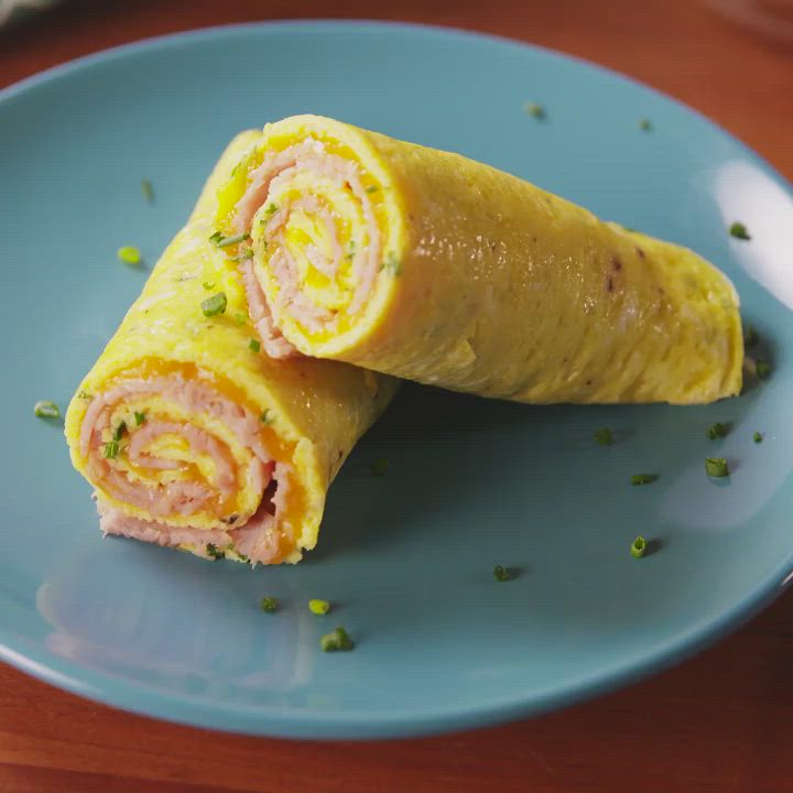 This may contain: a blue plate topped with an omelet roll on top of a wooden table