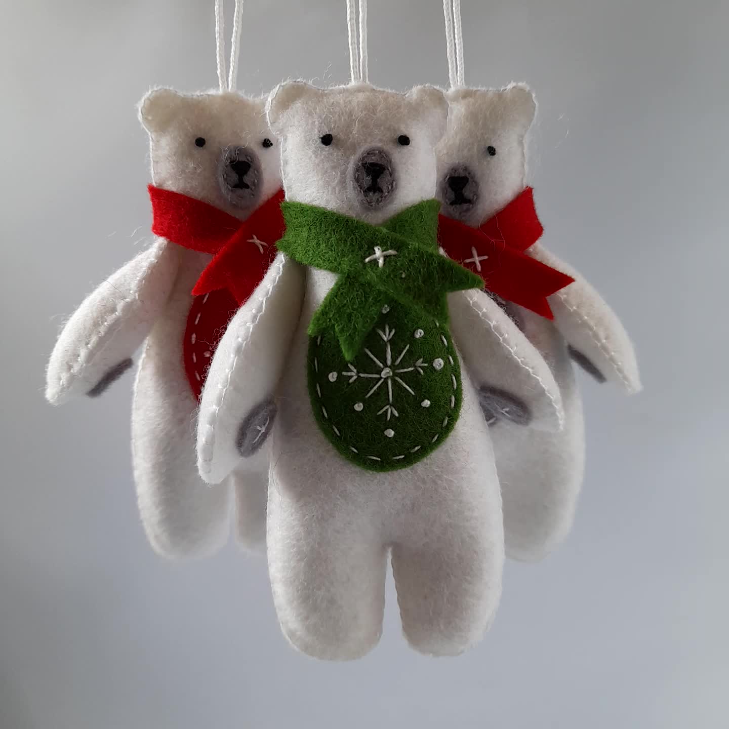 This may contain: three white teddy bears hanging from strings with red and green decorations on them's hands