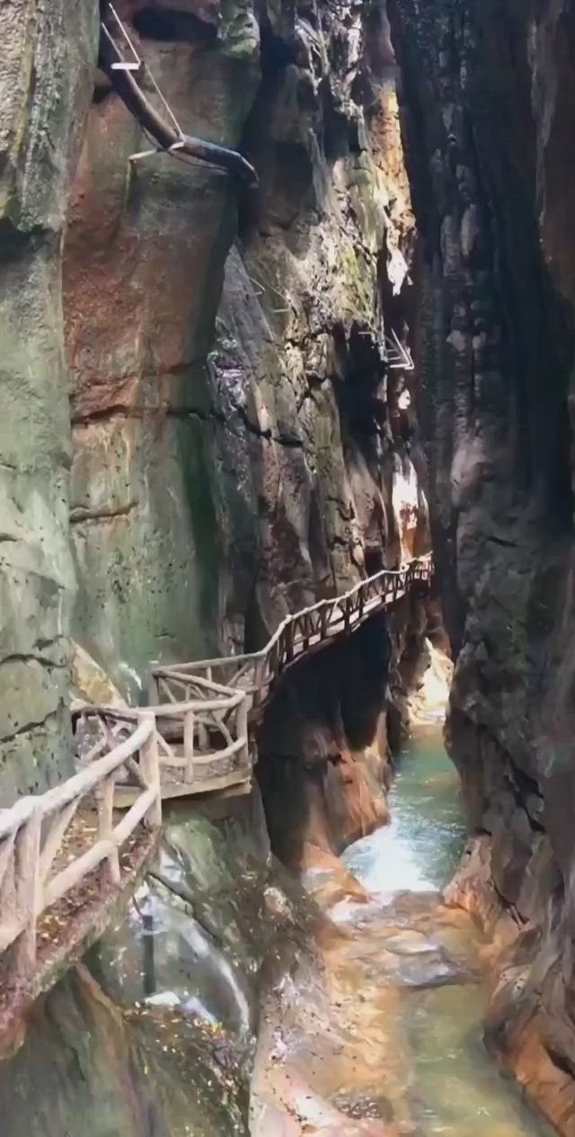 This may contain: a wooden bridge over a small stream in a canyon