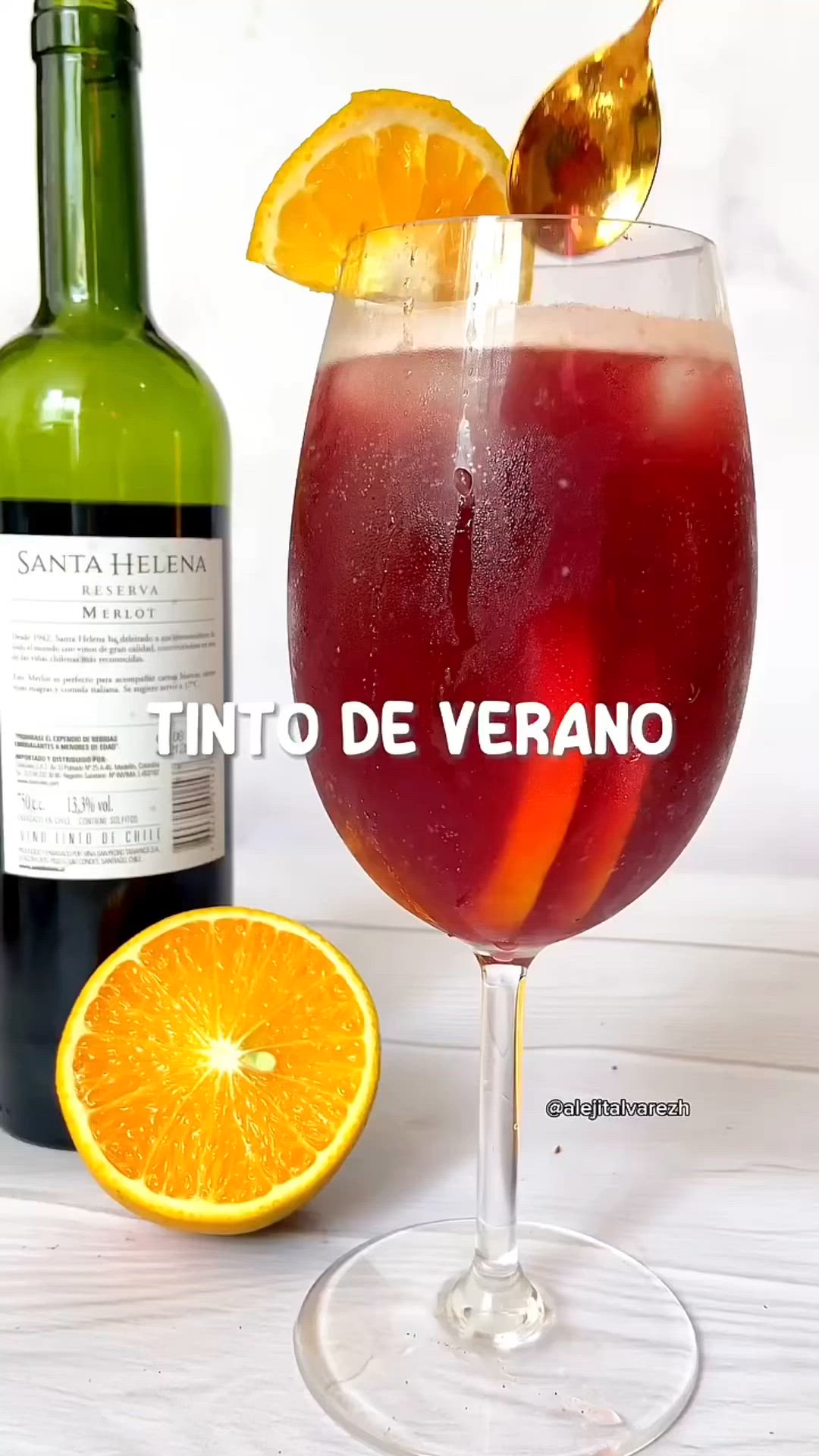 This may contain: a wine glass filled with liquid next to an orange slice and a bottle of wine