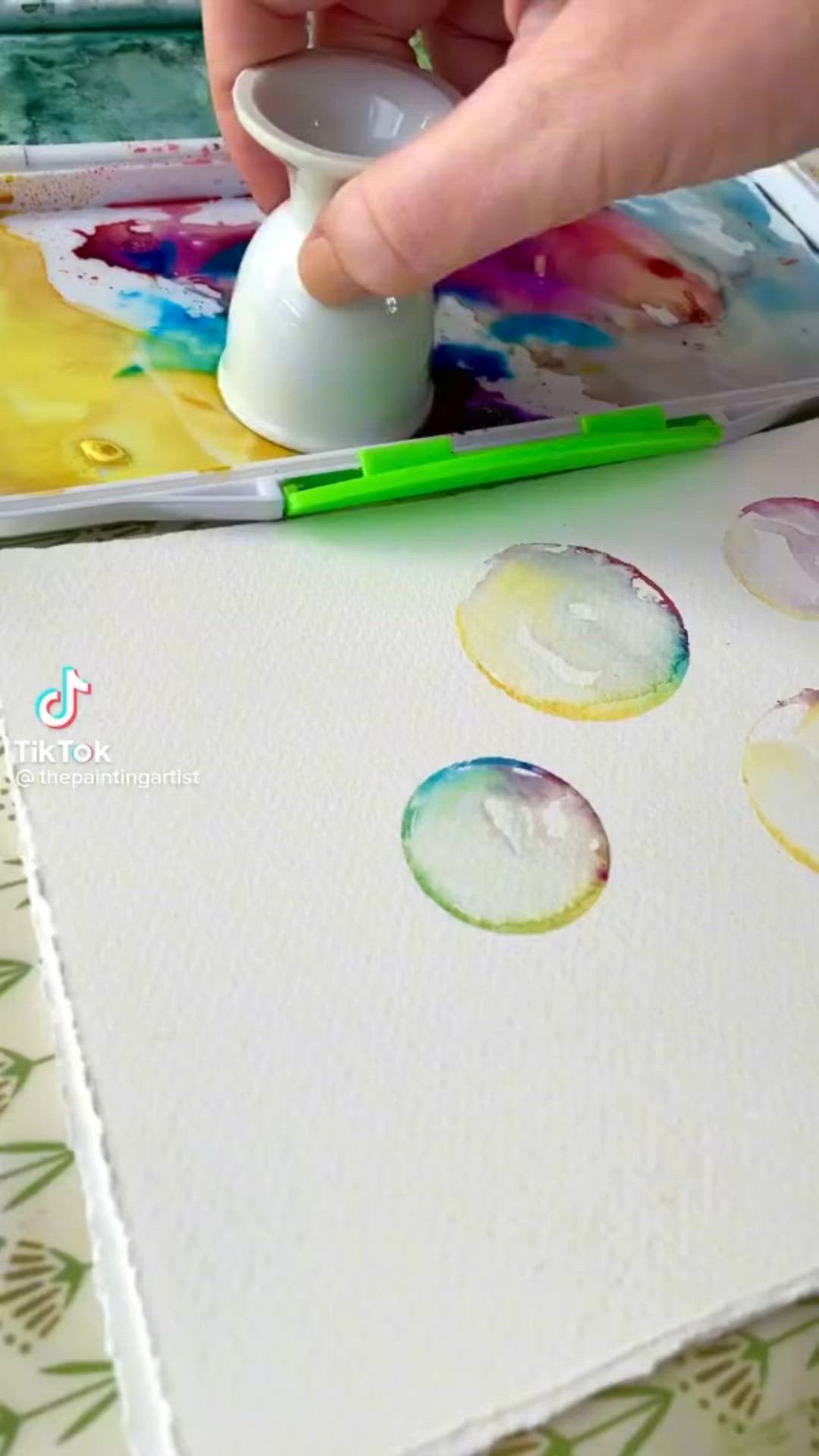 This may contain: a person is painting with watercolors on paper and using a glue pen to paint circles