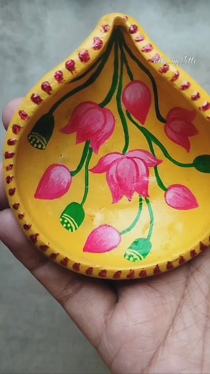 This may contain: a hand holding a yellow bowl with pink flowers painted on the side and green leaves