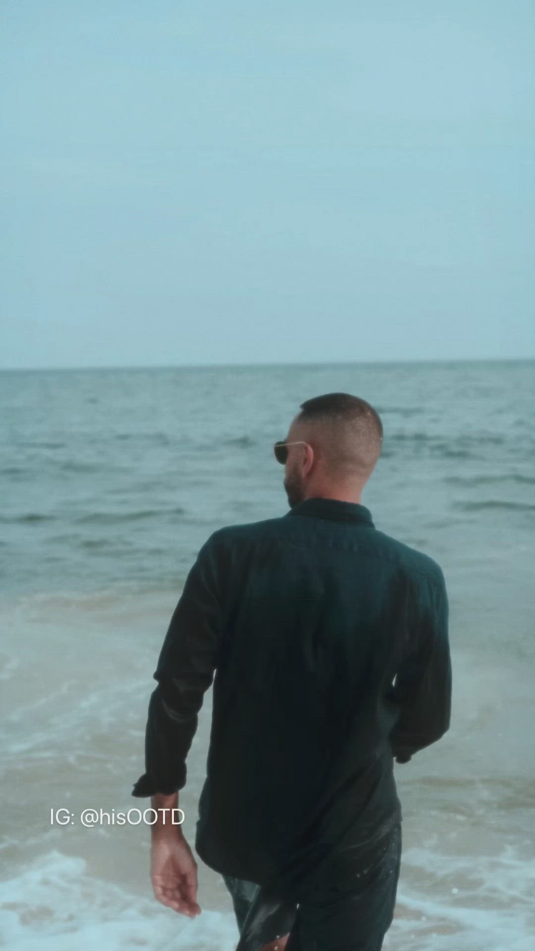 This may contain: a man walking on the beach with his back to the camera