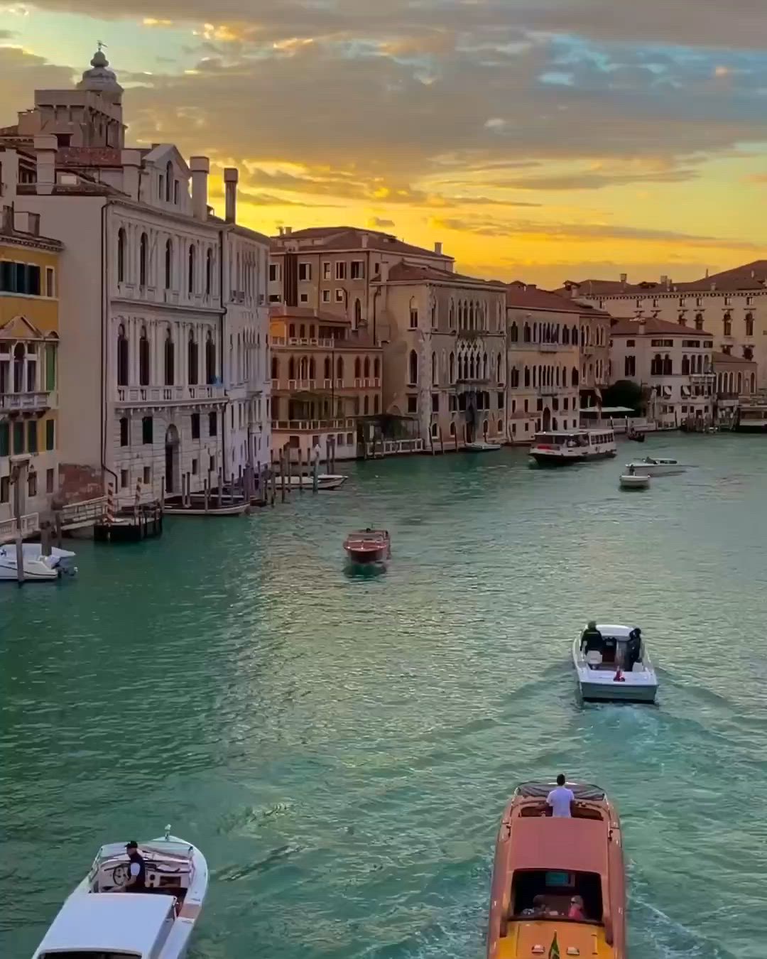 This may contain: several boats are traveling down the canal in venice, italy at sunset or sunrise time