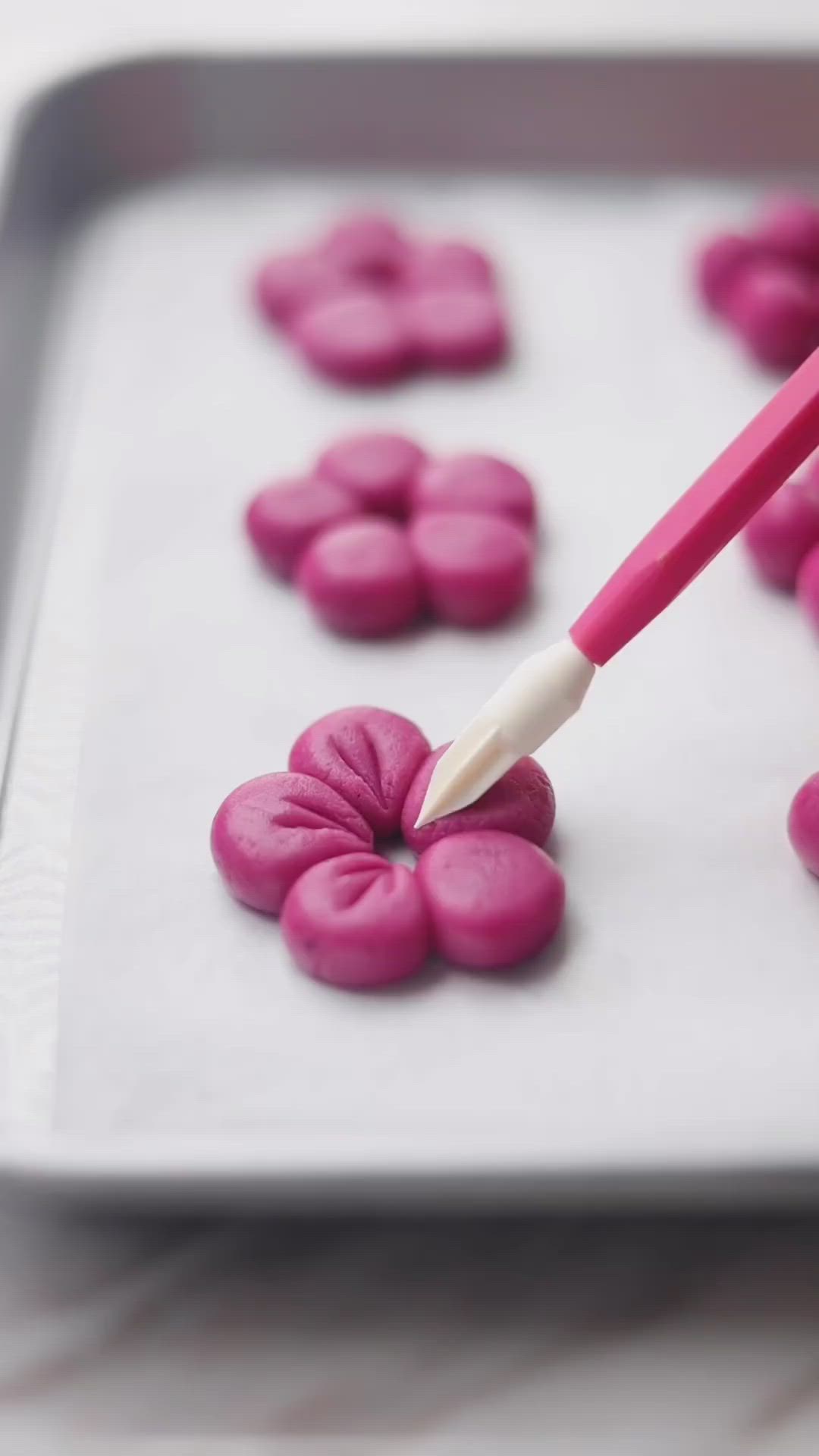 This may contain: two hands holding pink and white flowers in front of a plate with cookies on it