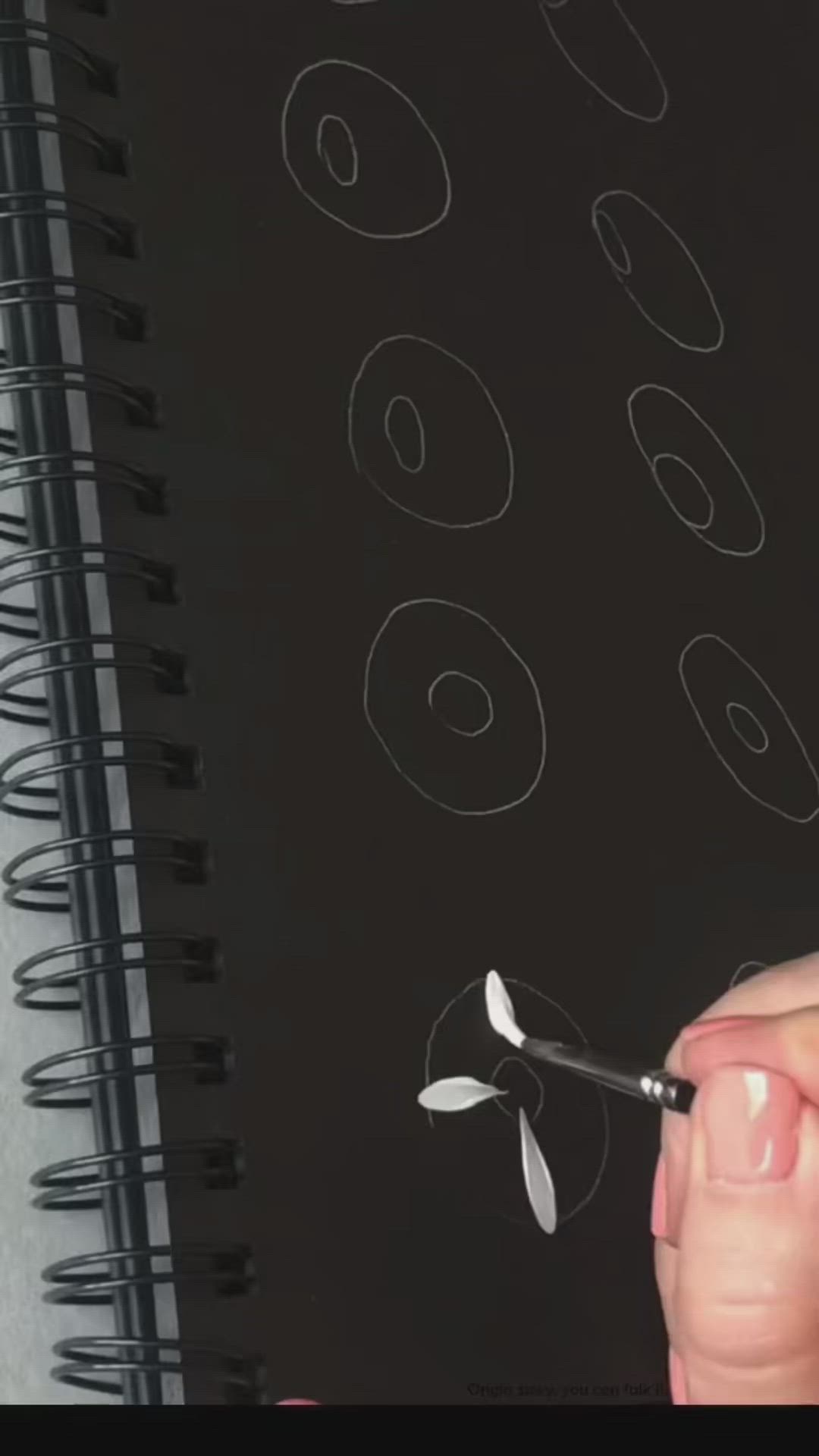 This may contain: someone is using a marker to draw flowers on a black paper with white outlines