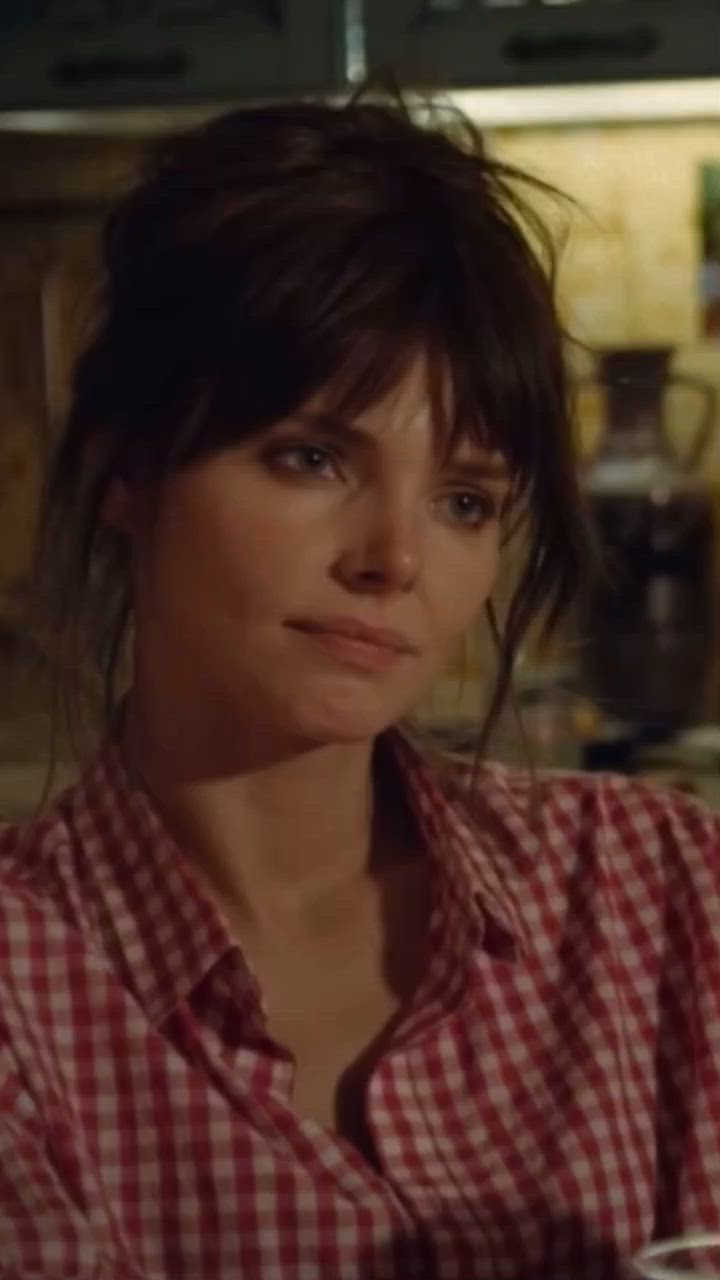 This may contain: a woman in a red and white checkered shirt sitting at a table with a cup