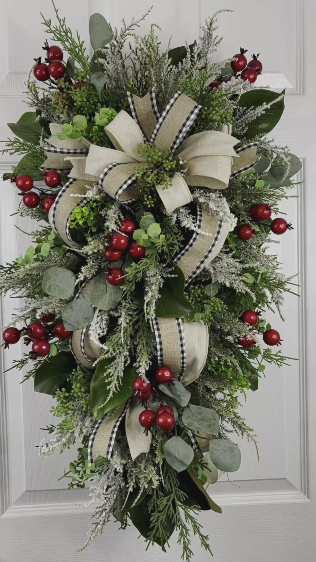 This may contain: a christmas wreath with berries and greenery hanging on the front door for holiday decor