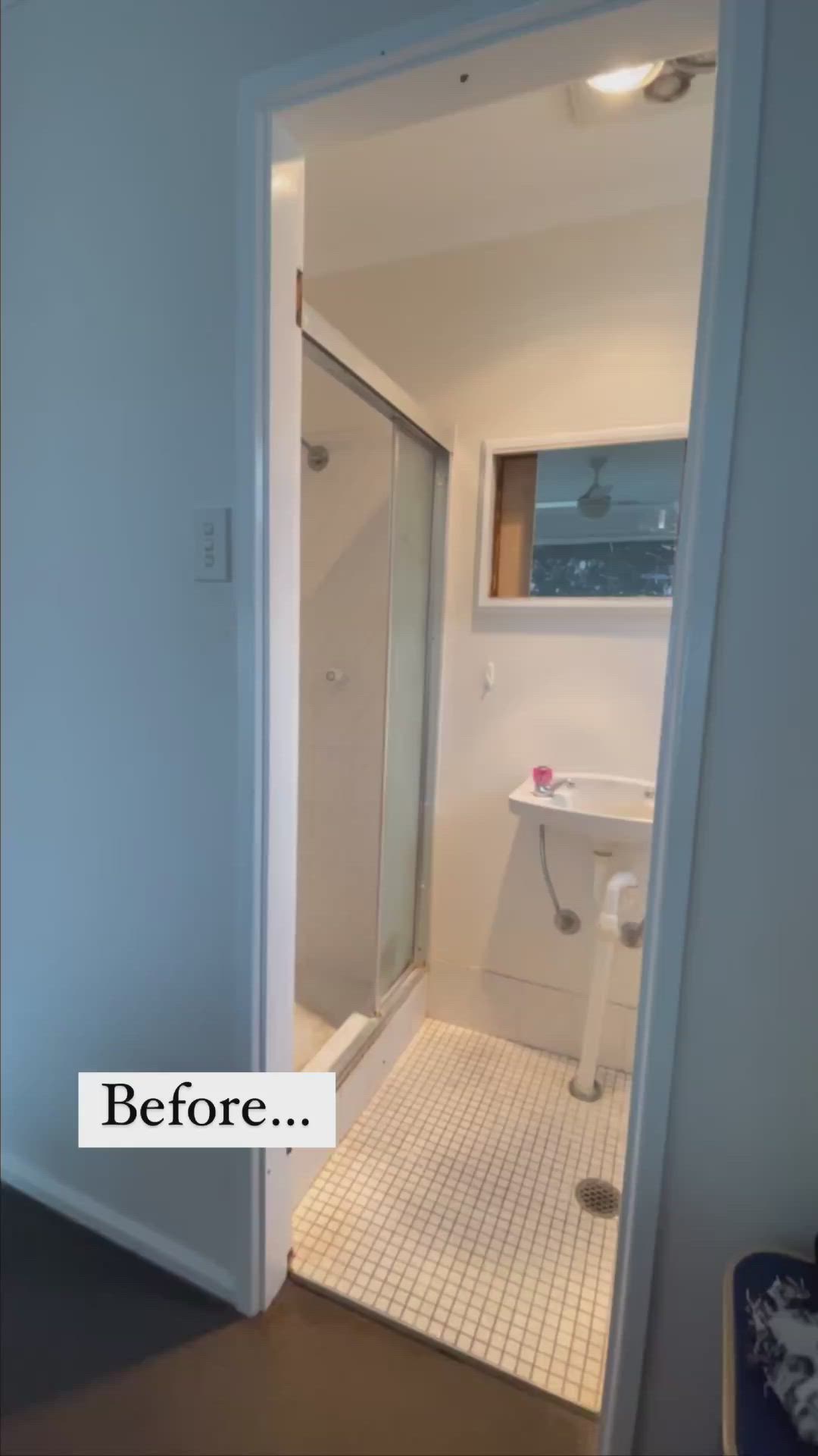 This may contain: a bathroom with a glass shower door next to a white sink and wooden counter top