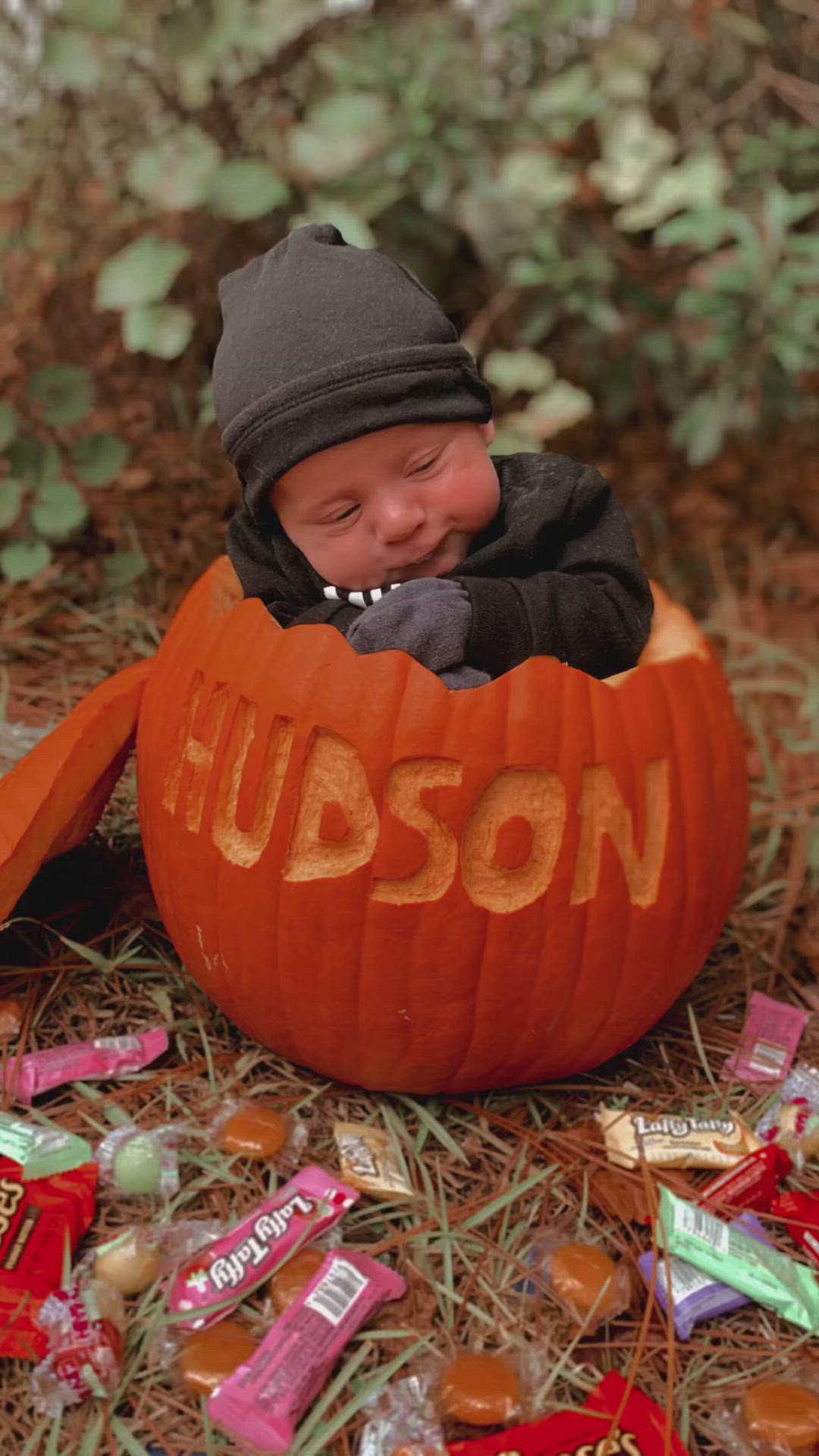 This may contain: a baby in a pumpkin with the word hudson carved into it's face and surrounded by candy