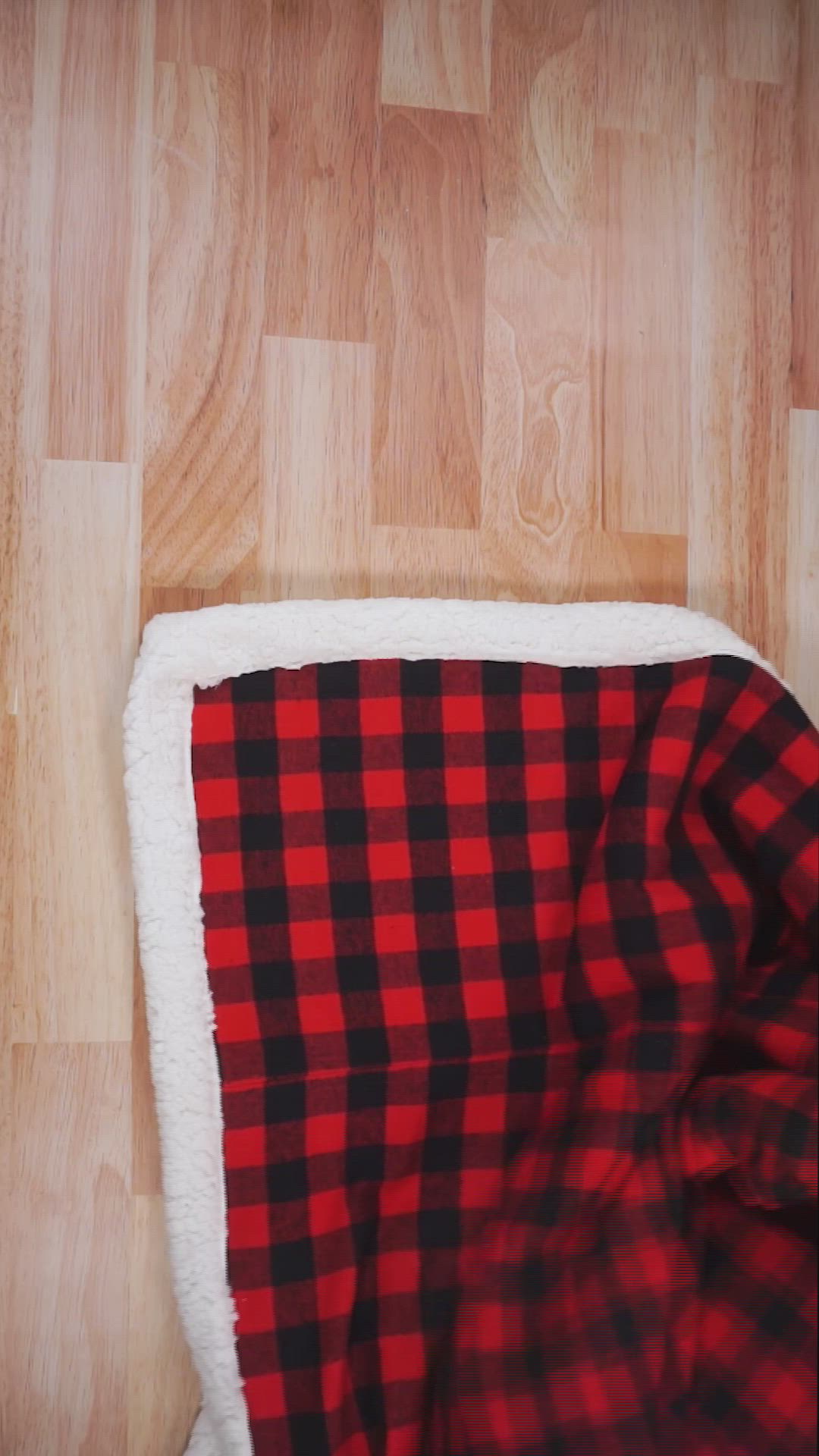 This may contain: a red and black plaid blanket laying on top of a wooden floor