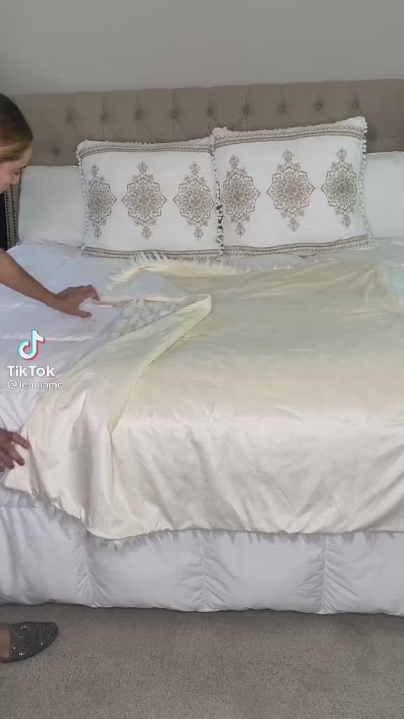 This may contain: a woman in black shirt laying on bed with white comforter and pillowcases