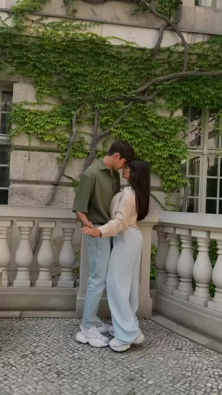 This may contain: a man and woman standing next to each other in front of a building with ivy growing on it