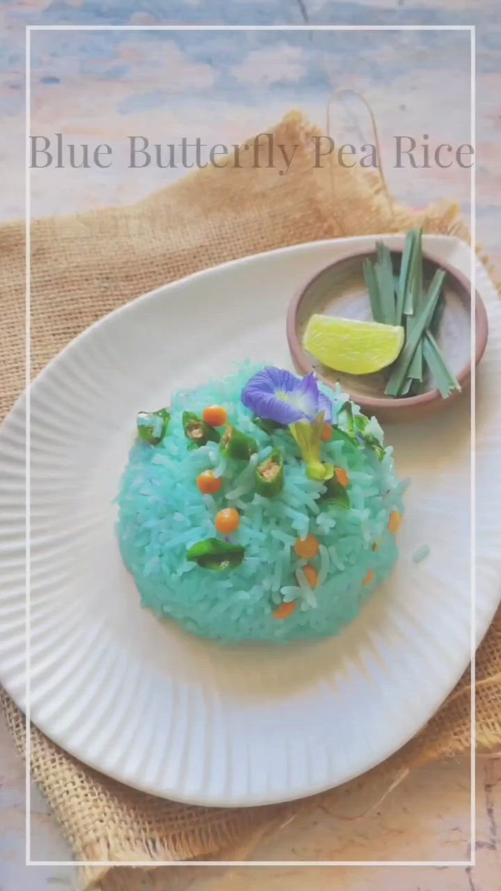 This may contain: a white plate topped with rice covered in blue and purple flowers next to a small bowl of green beans