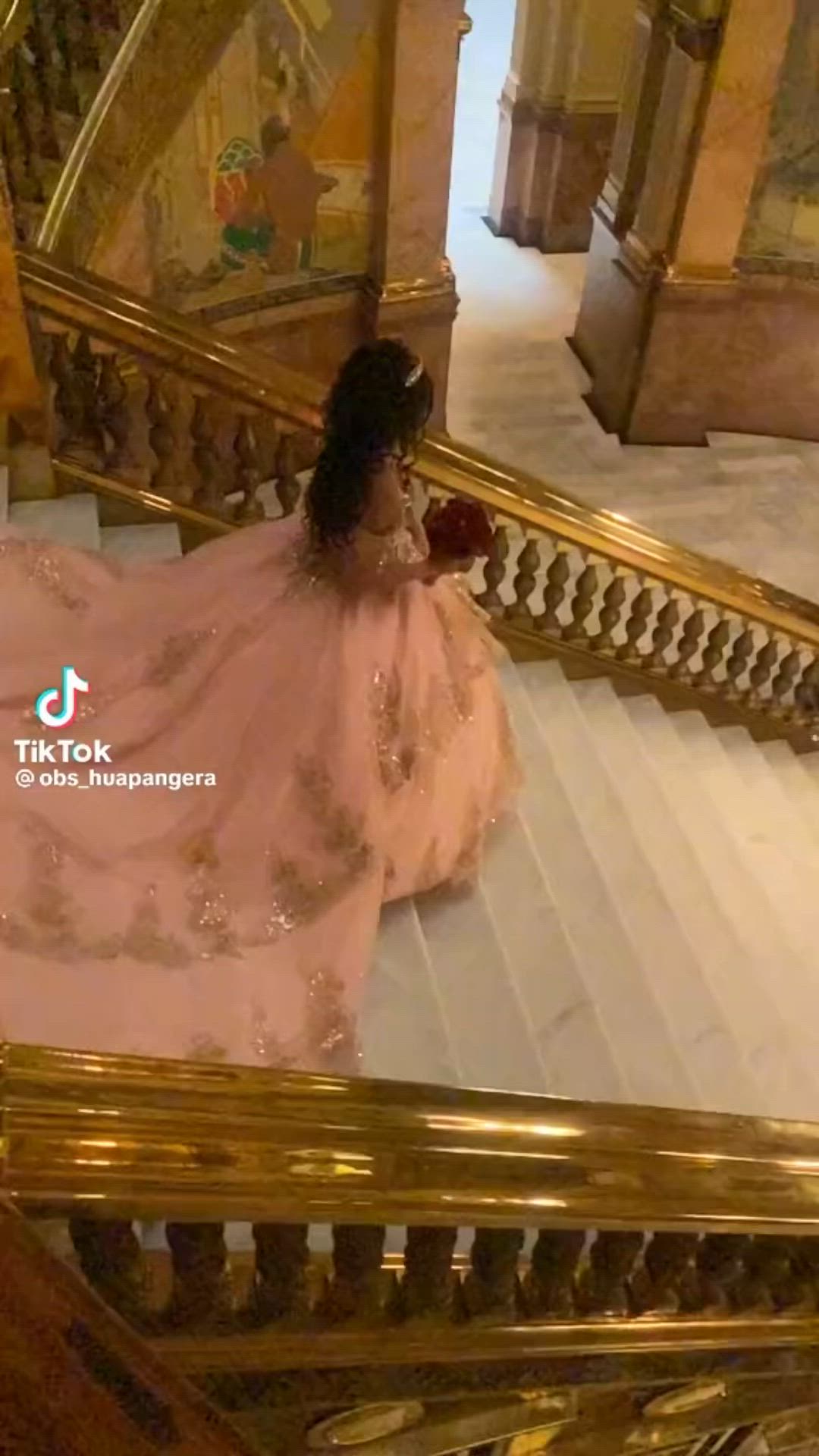 This may contain: a woman in a pink dress is sitting on the stairs