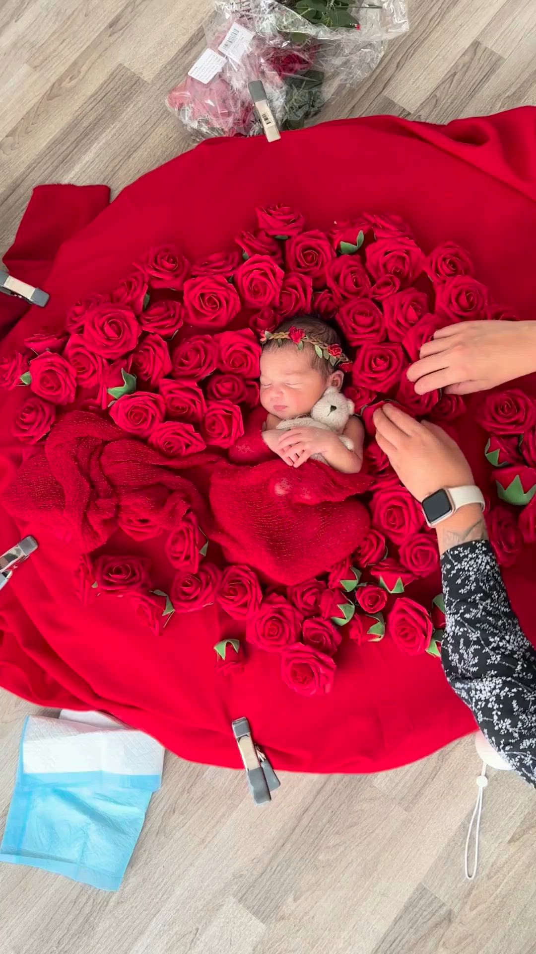 This may contain: a woman holding a baby on top of a red rose covered blanket with roses in the shape of a heart