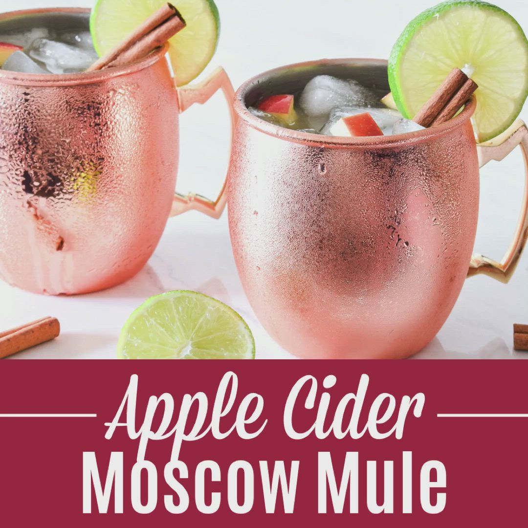 This may contain: two copper mugs filled with apple cider moscow mule and cinnamon stick garnish