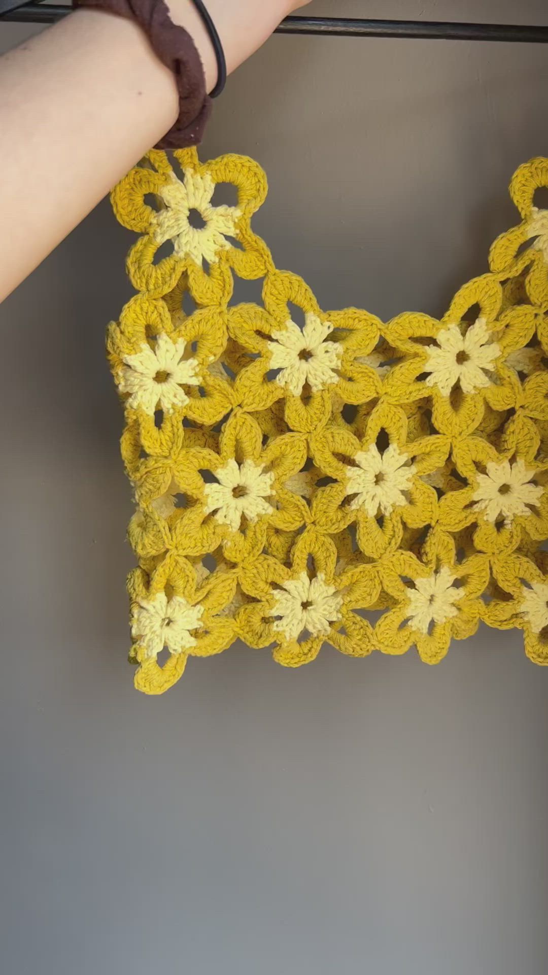 This may contain: a yellow crocheted doily is hanging on a clothes line with a woman's hand