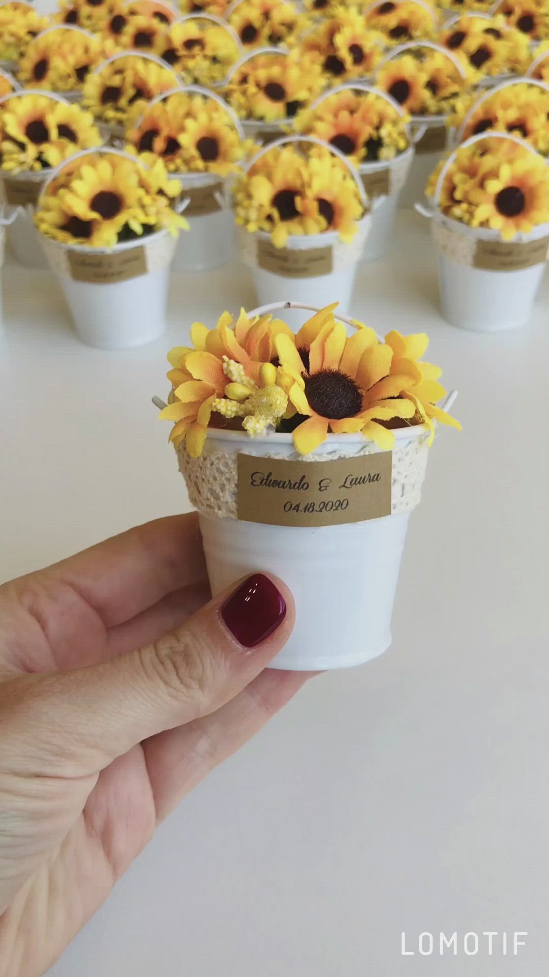 This may contain: a hand holding a cup with sunflowers in it on top of a table