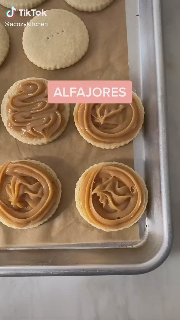 This may contain: cookies with peanut butter in the middle on a baking sheet that says alfajores