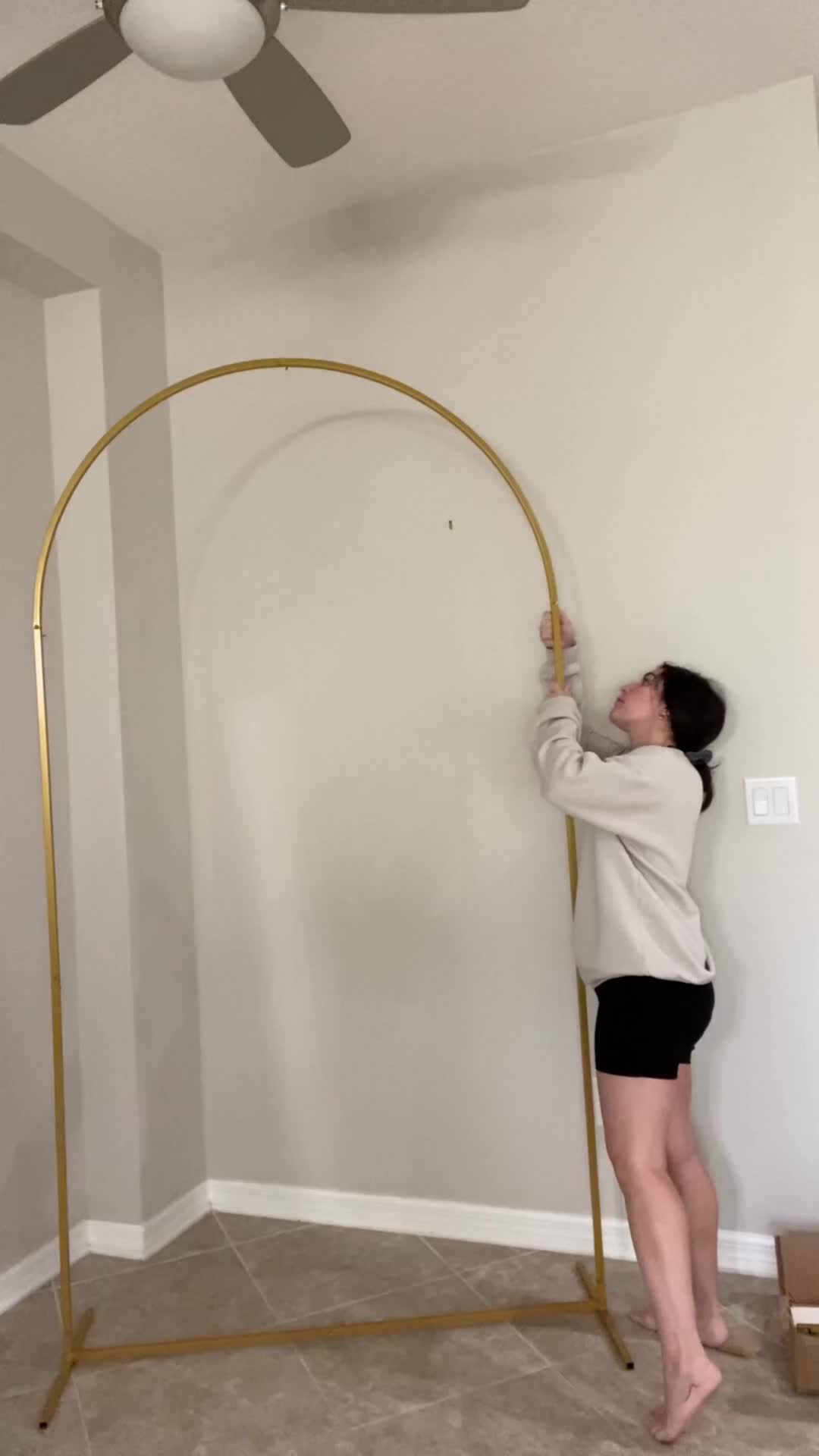 This may contain: a woman standing in front of a ceiling fan and holding onto a large metal frame