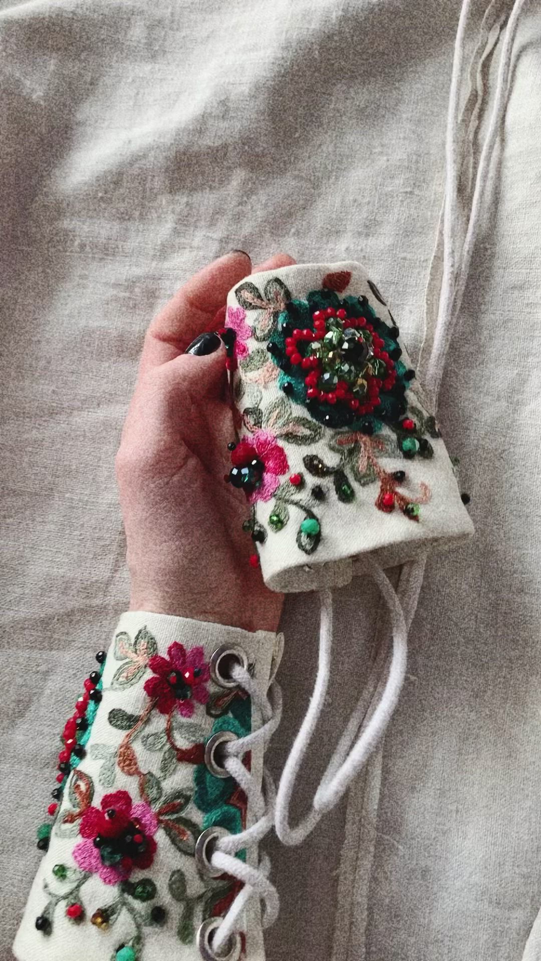 This may contain: a woman's hand is holding a white case with flowers and beads on it