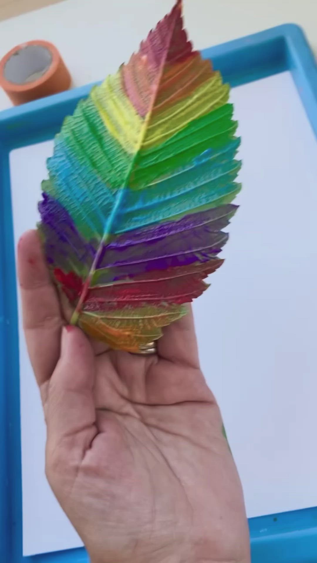 This may contain: a child's handprinted leaf on a white paper and blue tray with green leaves