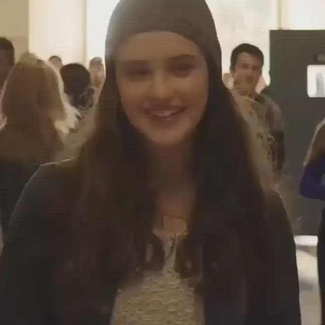 This may contain: a woman with long hair wearing a beanie smiles at the camera while standing in front of other people