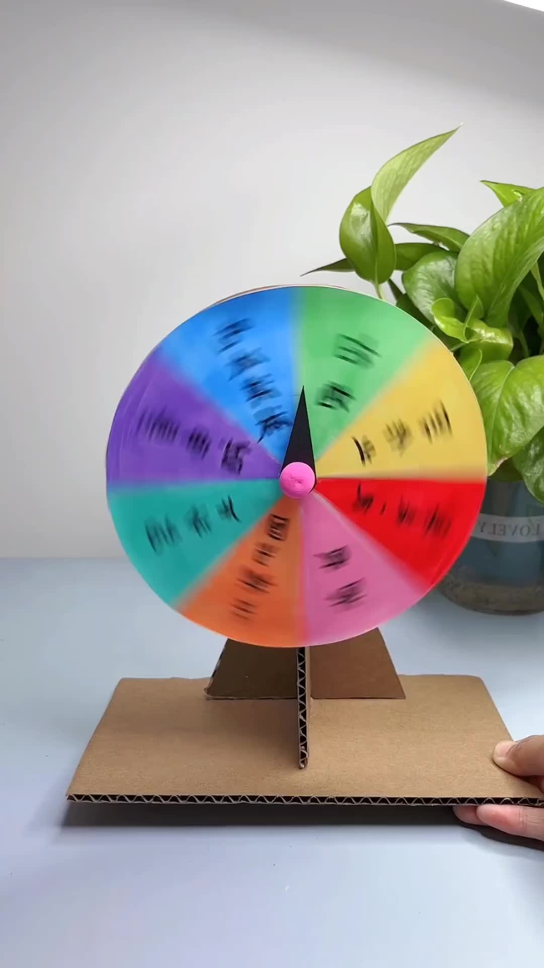 This may contain: a hand holding a colorful wheel on top of a wooden stand next to a potted plant