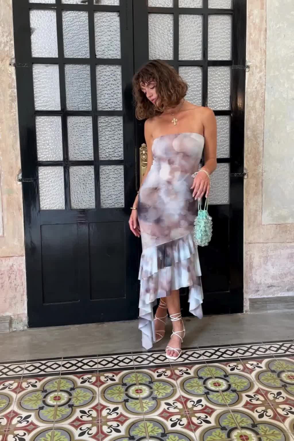 This may contain: a woman standing in front of a door wearing a strapless dress and holding a handbag