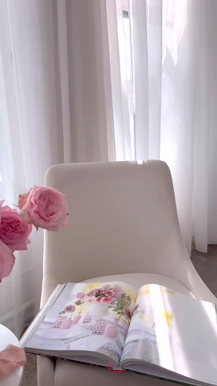 This may contain: pink roses in a basket sitting on a table next to a white chair and window