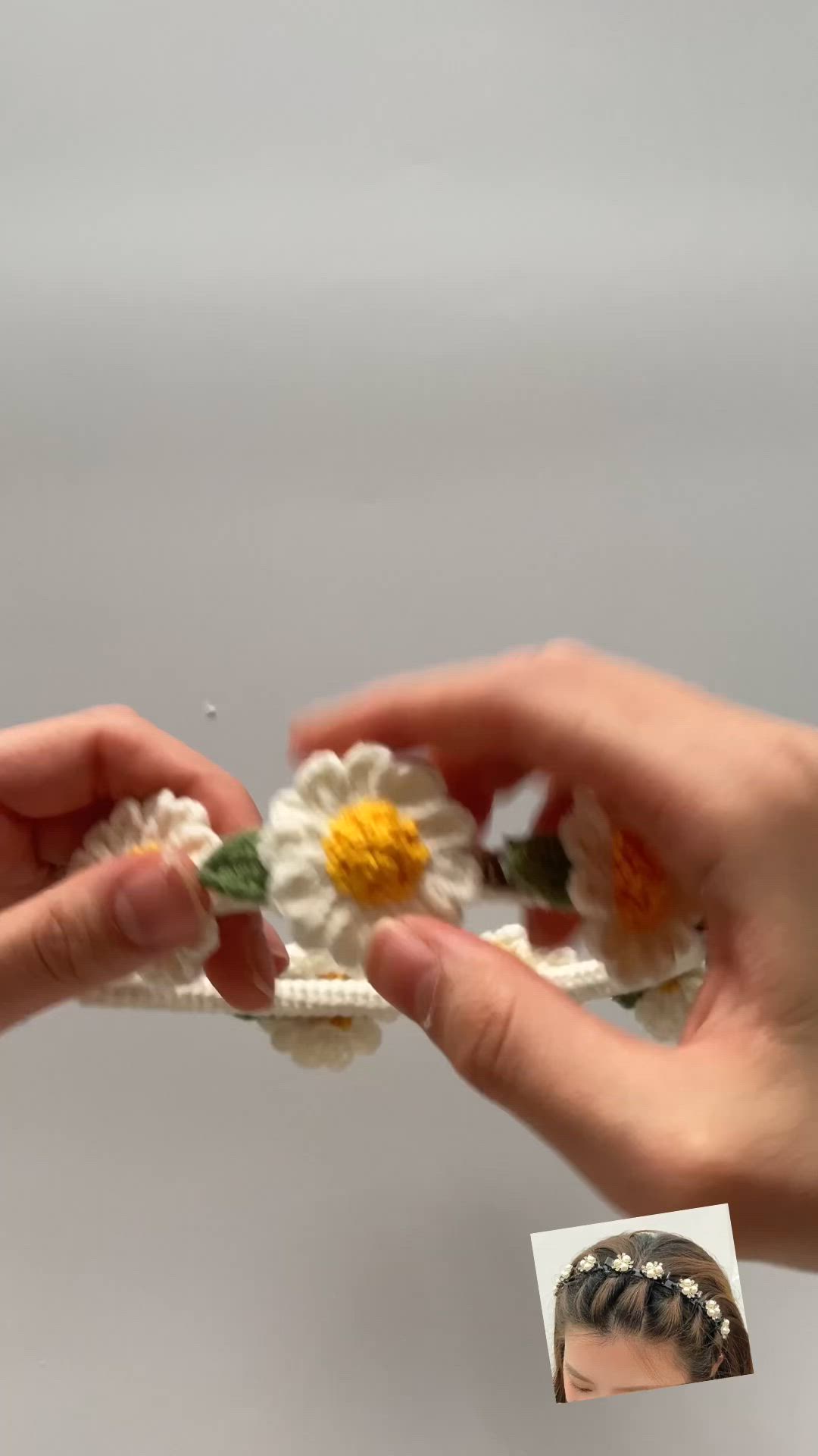 This may contain: a hand holding a crocheted headband with daisies on it