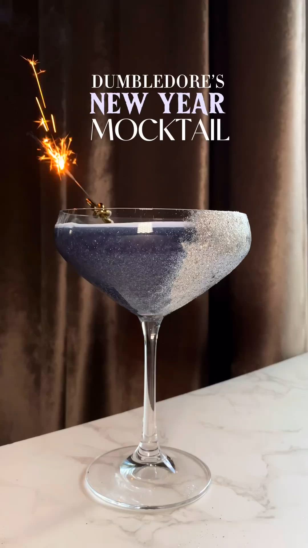 This may contain: a blue cocktail in a glass with a sparkler sticking out of the top and text that reads dumbledore's new year mocktail