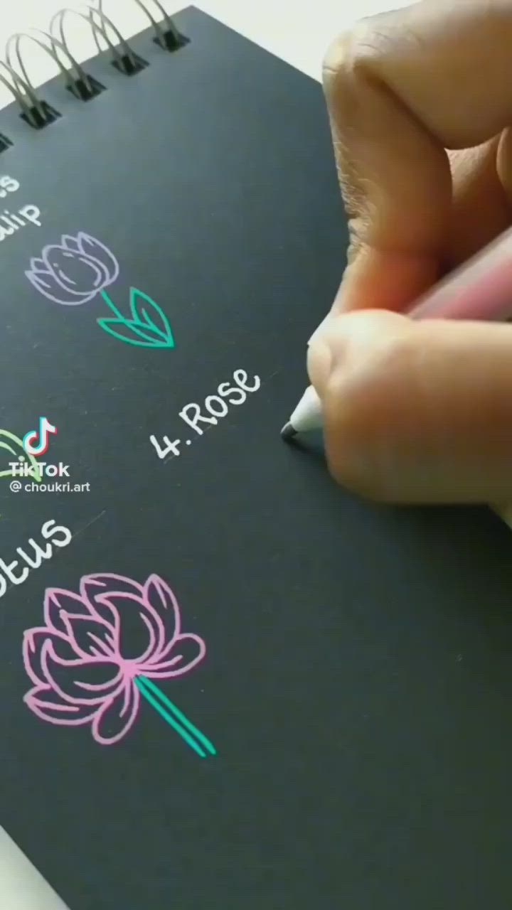 This may contain: a person is writing on a notebook with flowers drawn on the pages and in different colors