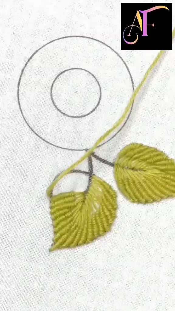 This may contain: a close up of a piece of cloth with two leaves on it and a circular design in the middle