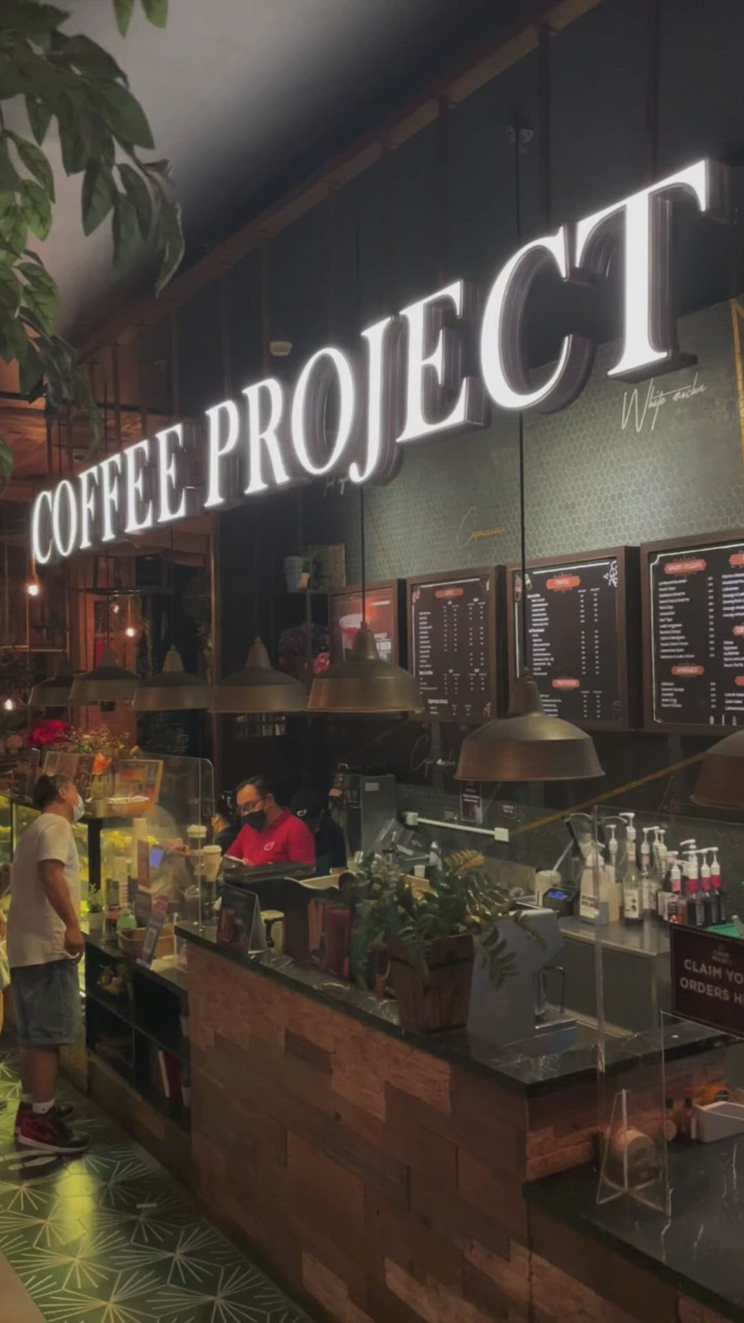 This may contain: people are standing in front of the coffee project sign and counter area at night time