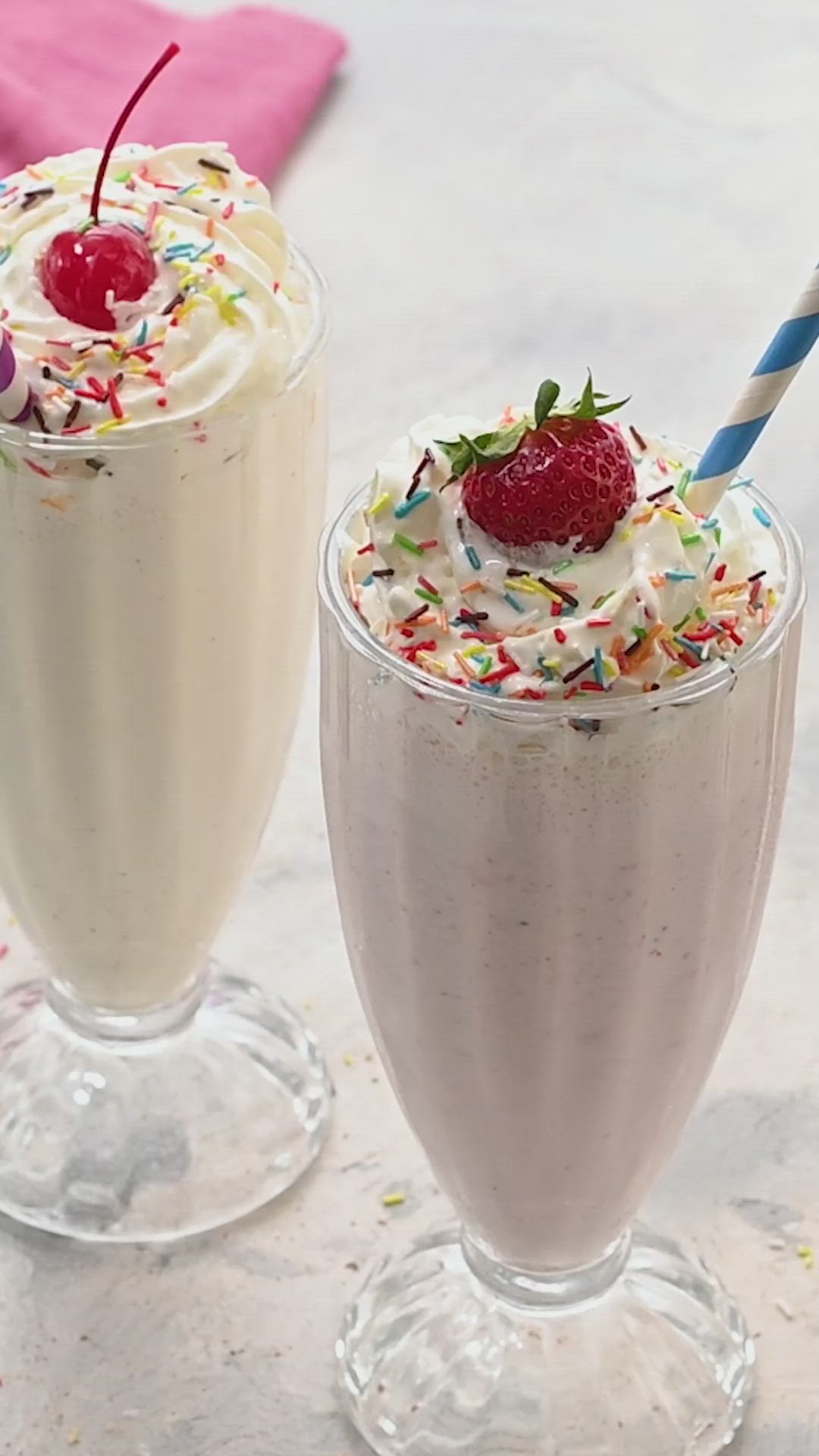 This may contain: two milkshakes with strawberries and sprinkles on them