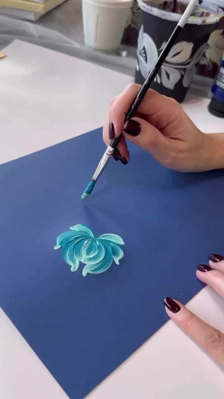 This may contain: a woman is using a paintbrush to create an acrylic design on a piece of paper