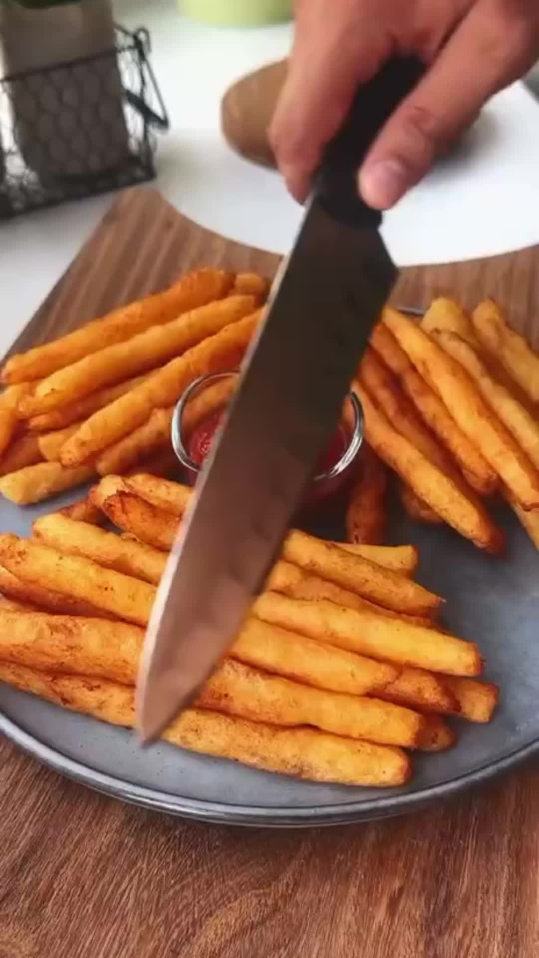 This may contain: a person is holding a knife over some french fries on a plate with ketchup