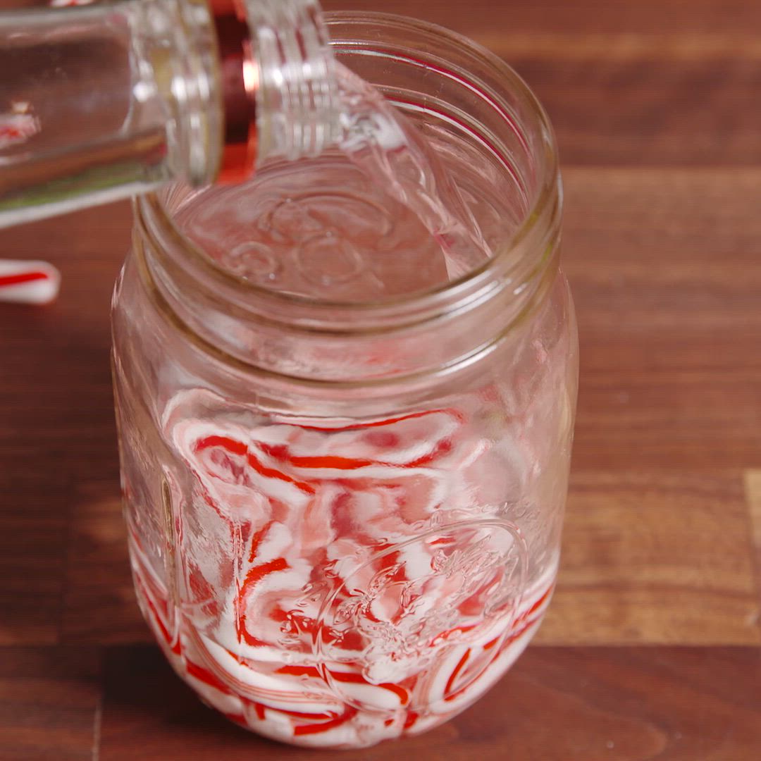 This may contain: two hot chocolate drinks with whipped cream and candy canes in their mugs, being held by someone's hand