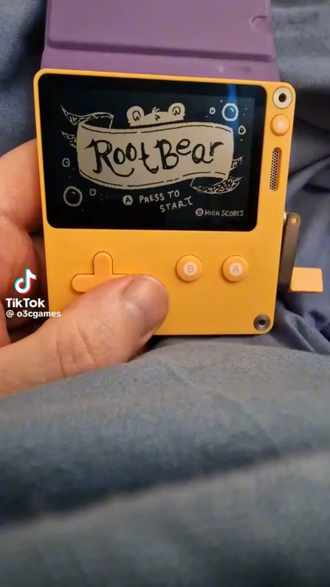 This may contain: a person holding an old fashioned gameboy in their lap with the screen showing rootbear